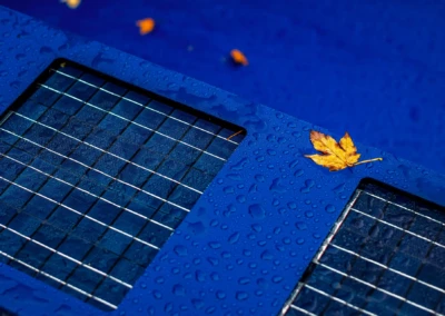 Chez-Elizabeth-et-Jacques-5 Blauw zonnepaneel met waterdruppels en gele herfstblad op een blauwe achtergrond.