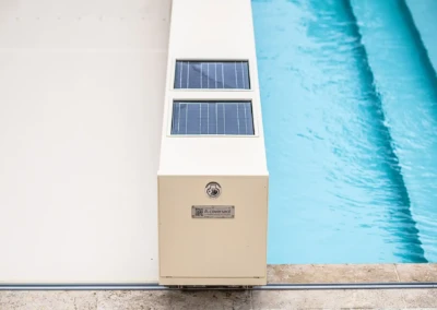 Chez-Camille-et-Arthur-6 Een beige behuizing met zonnepanelen is geïnstalleerd aan de rand van een blauw zwembad, omringd door stenen tegels.