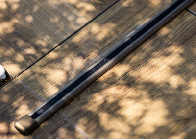 Schaduwen van bomen op een lichte houten vloer met een zwarte metalen staaf die door het beeld loopt.