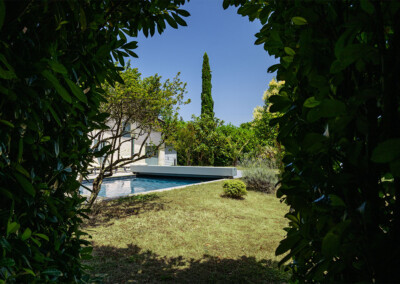 Uitzicht op een zwembad omgeven door groen met een boom op de voorgrond en een blauwe lucht op de achtergrond.